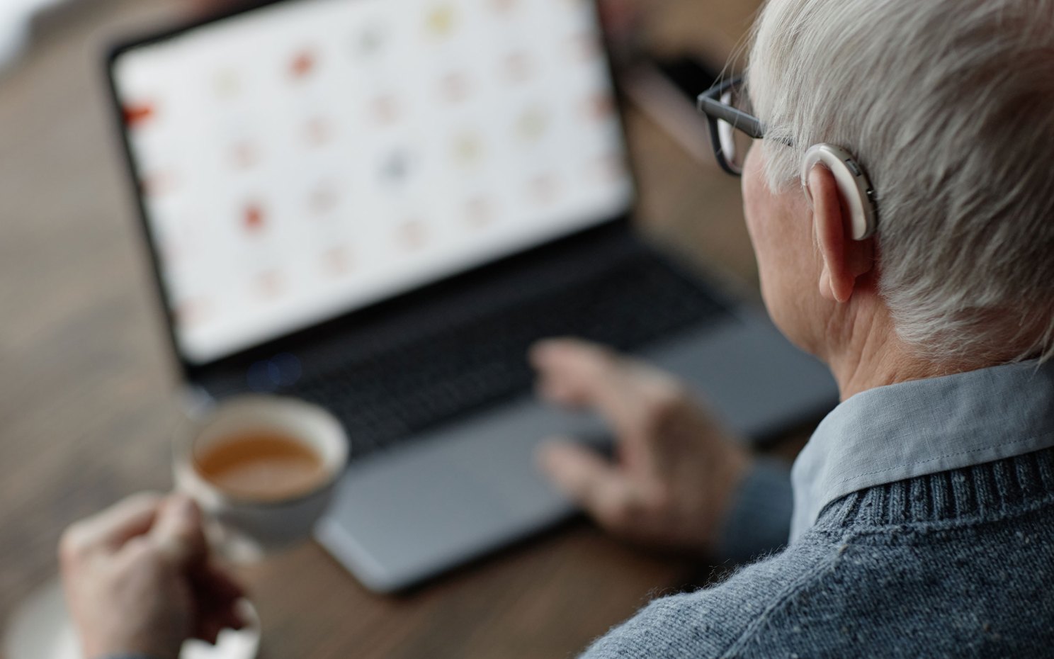 Over shoulder shot of older man wearing hearing aid while working on laptop.