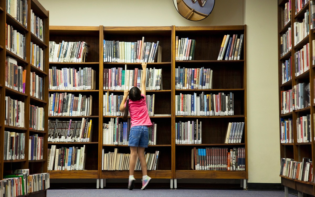Child stands on tip-toes to reach for a book off a shelf.