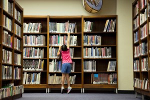 Child stands on tip-toes to reach for a book off a shelf.