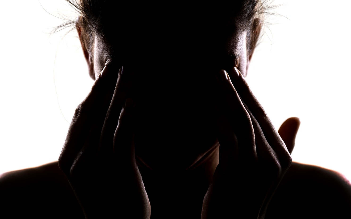 Silhouette of a person holding their head in their hands and rubbing their eyes.