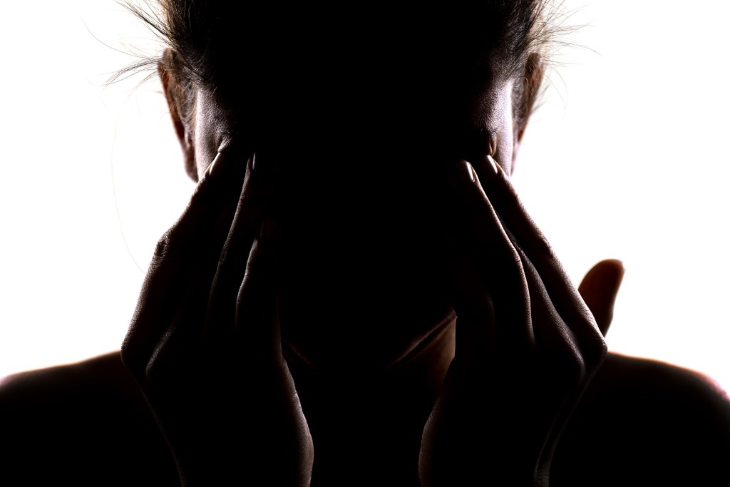 Silhouette of a person holding their head in their hands and rubbing their eyes.