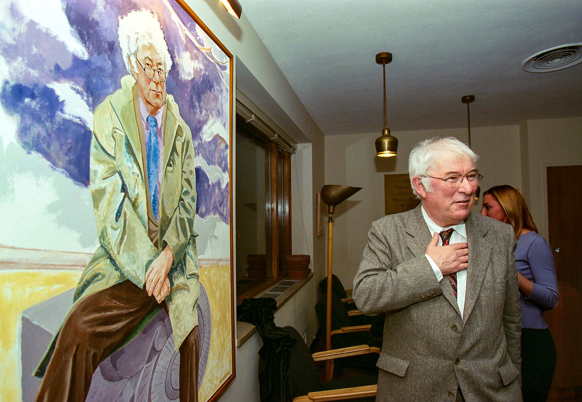Seamus Heaney hold his hand over his heart beside a portrait of himself unveiled in Lamont Library.