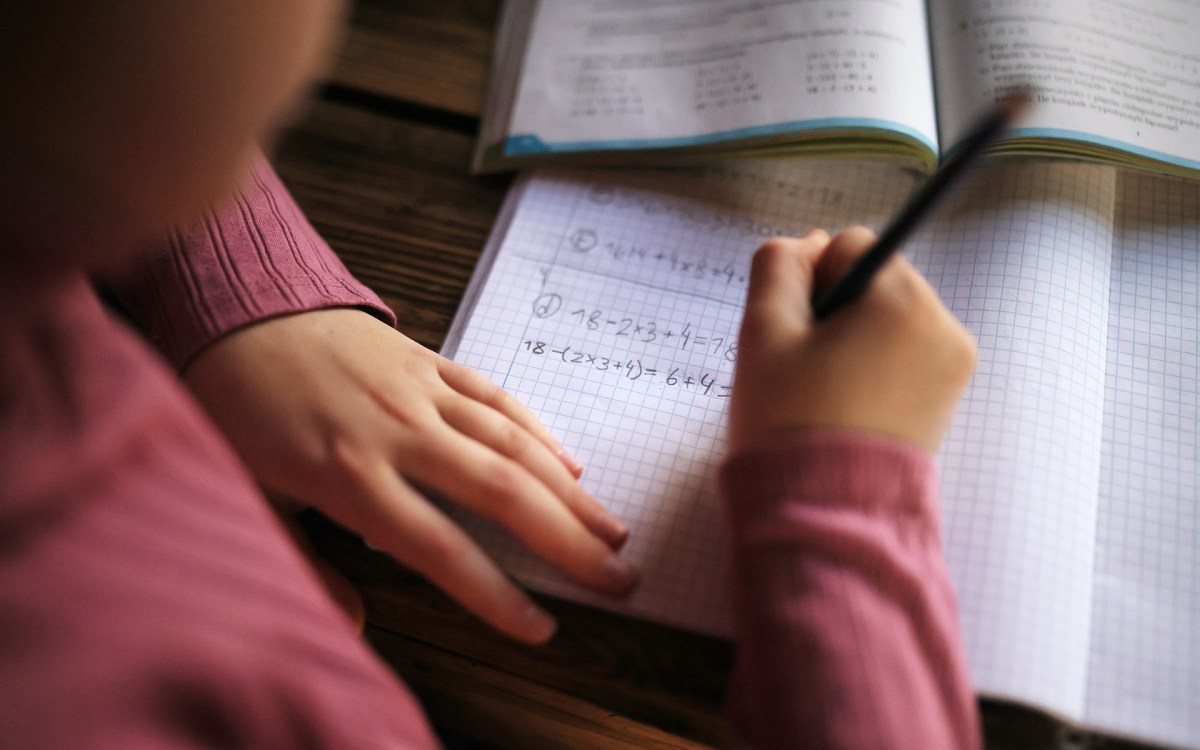 Close-up view on student's hand doing math homework in notebook.