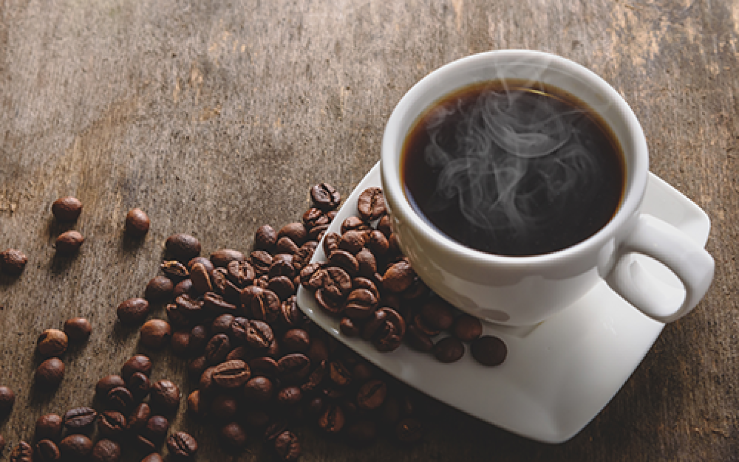 A steaming cup of coffee with coffee beans