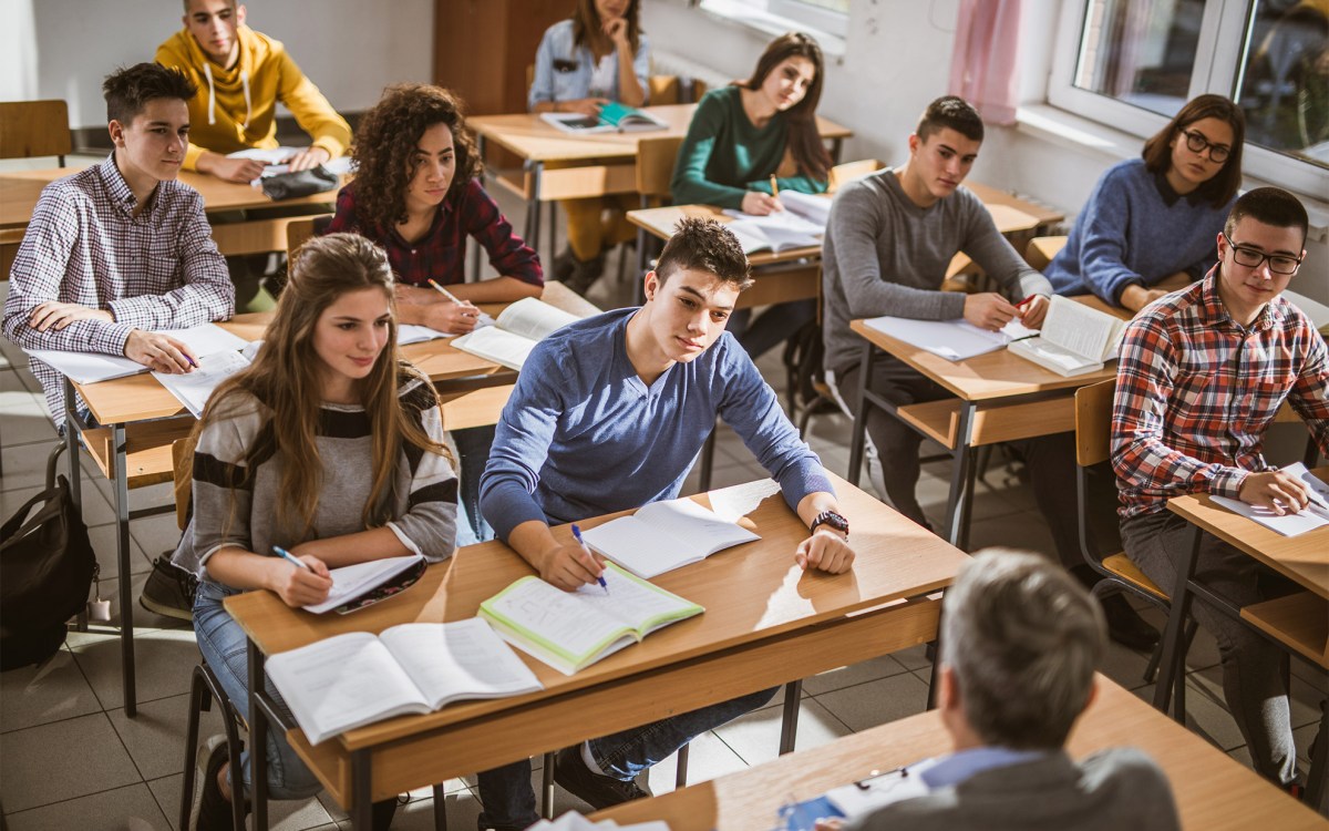 Large group of high school students listening to their teacher.