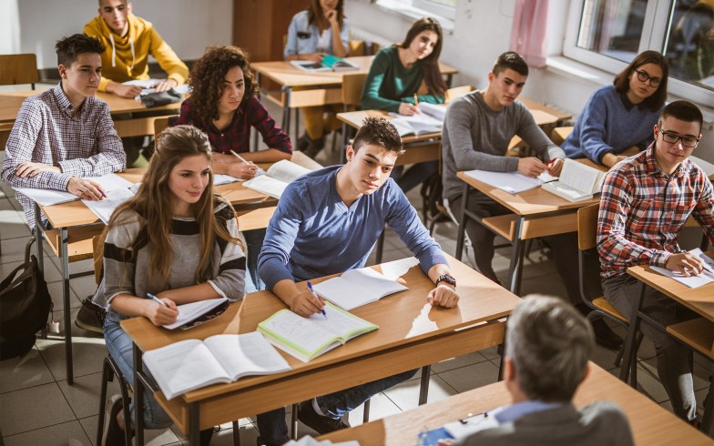 Large group of high school students listening to their teacher.