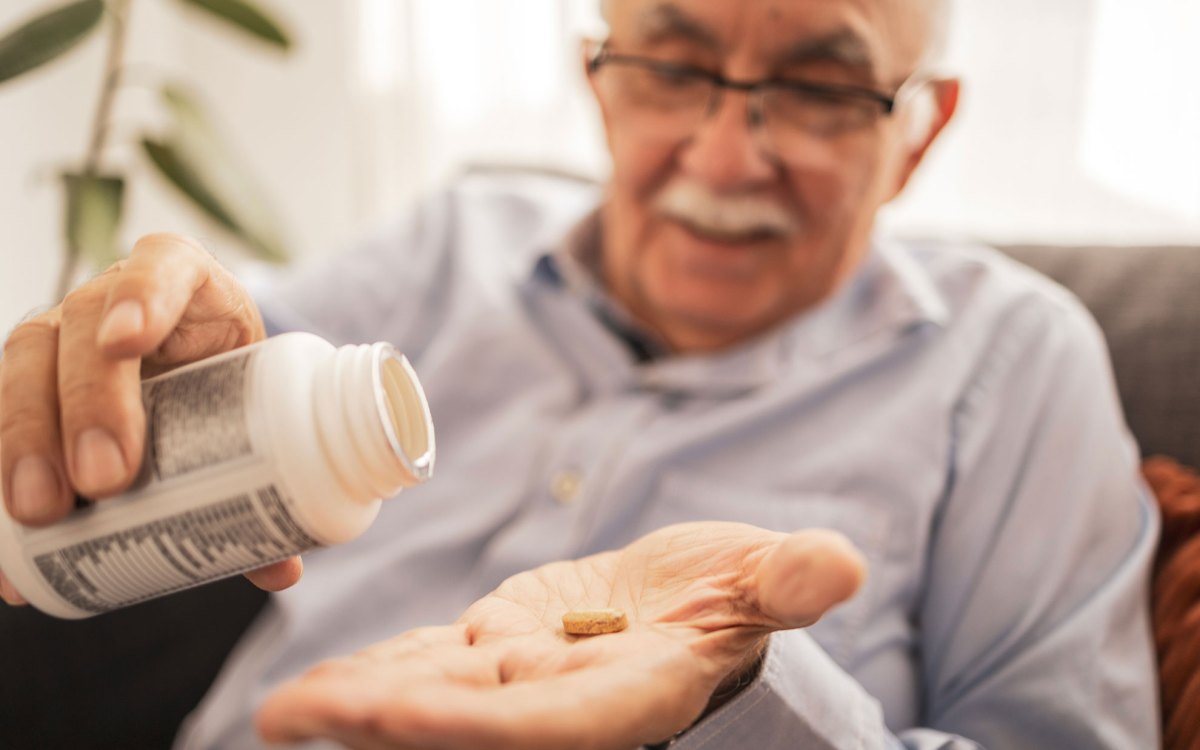 Elderly man holding a supplement pill in his palm.