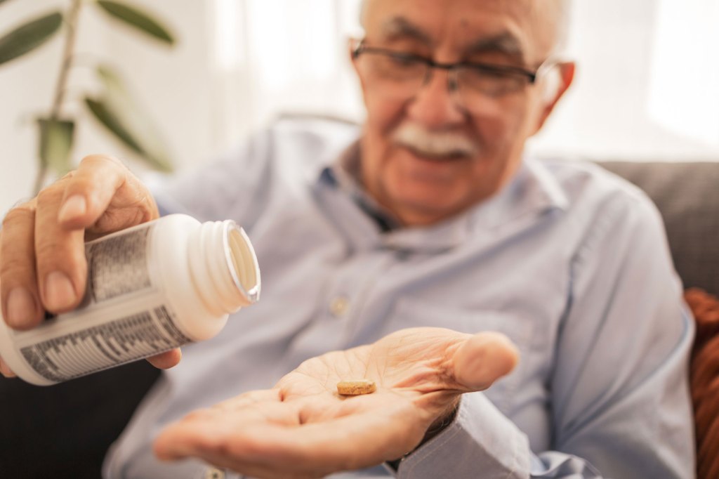 Elderly man holding a supplement pill in his palm.