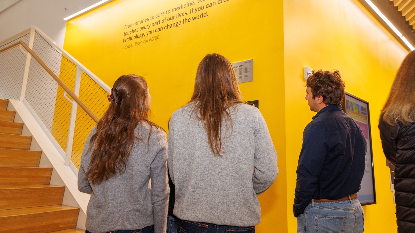 Members of the Troper Wojcicki family view a quote inscribed on the wall of the SEC leading to the Susan Wojcicki Library. The quote reads, "From phones to cars to medicine, technology touches every part of our lives. If you can create technology, you can change the world." 