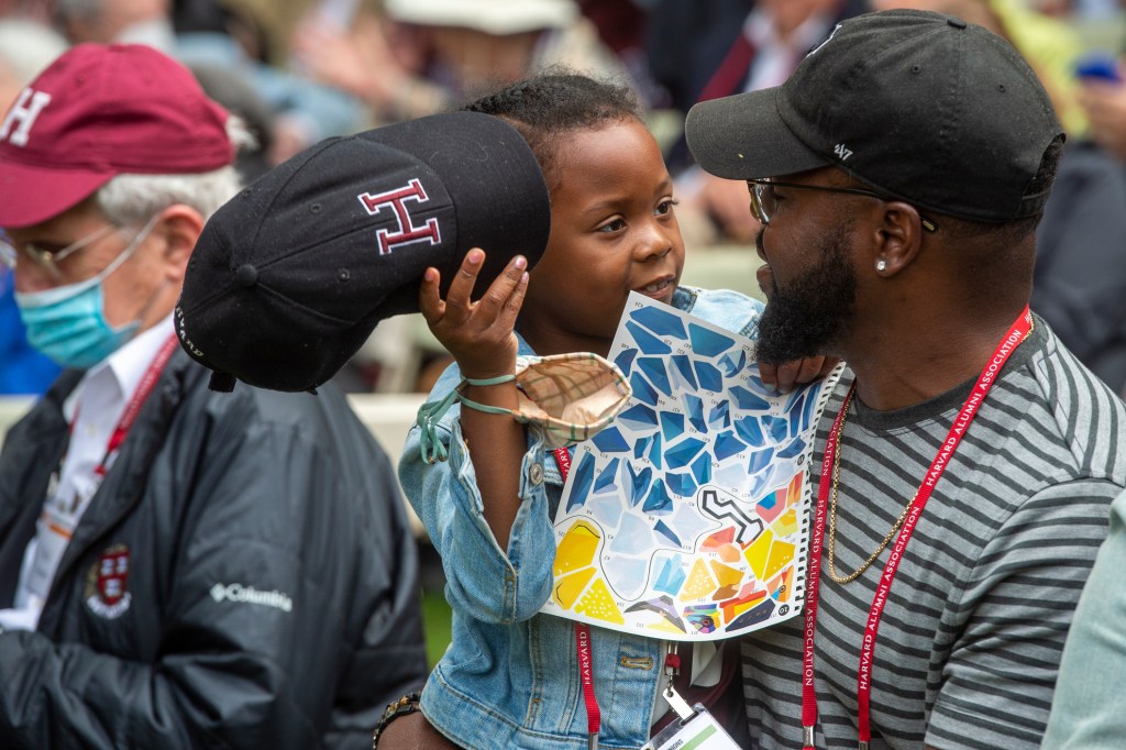 Nyla Dockery, 7, removes her Harvard hat while having a quiet conversation with her dad Prince Dockery '03, back for his 20th reunion on Harvard Alumni Day, 2022. 