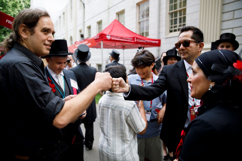 Justin Krebs '00 bumps fists with classmate Christopher Amar as they assemble for a parade in Old Yard during Harvard Alumni Day, 2025.