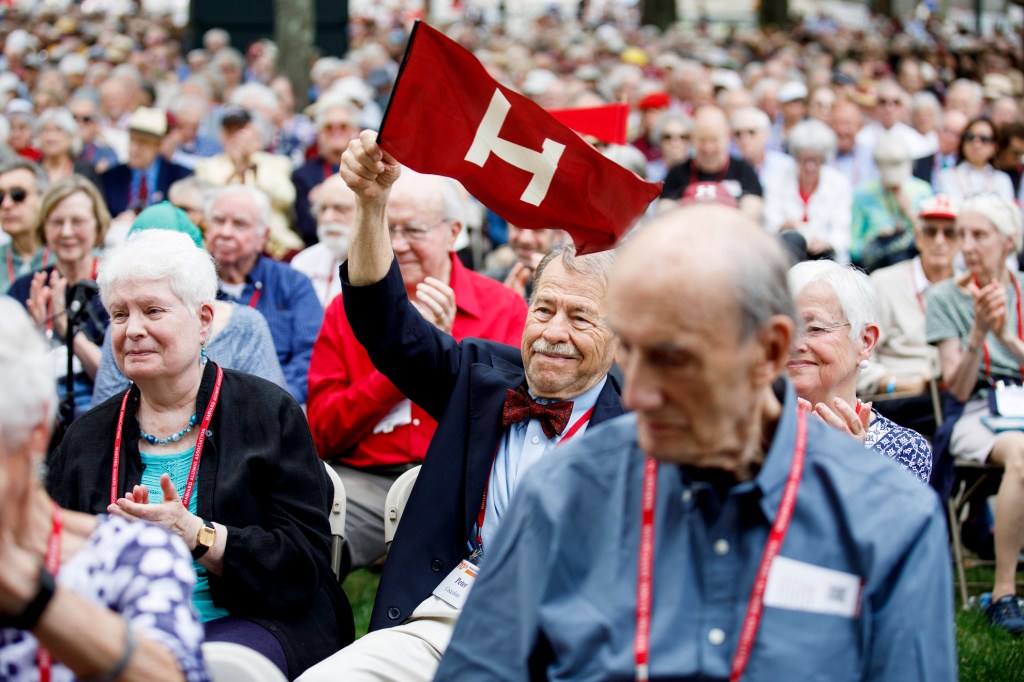 An audience member waves a Harvard flag on Harvard Alumni Day, 2025.