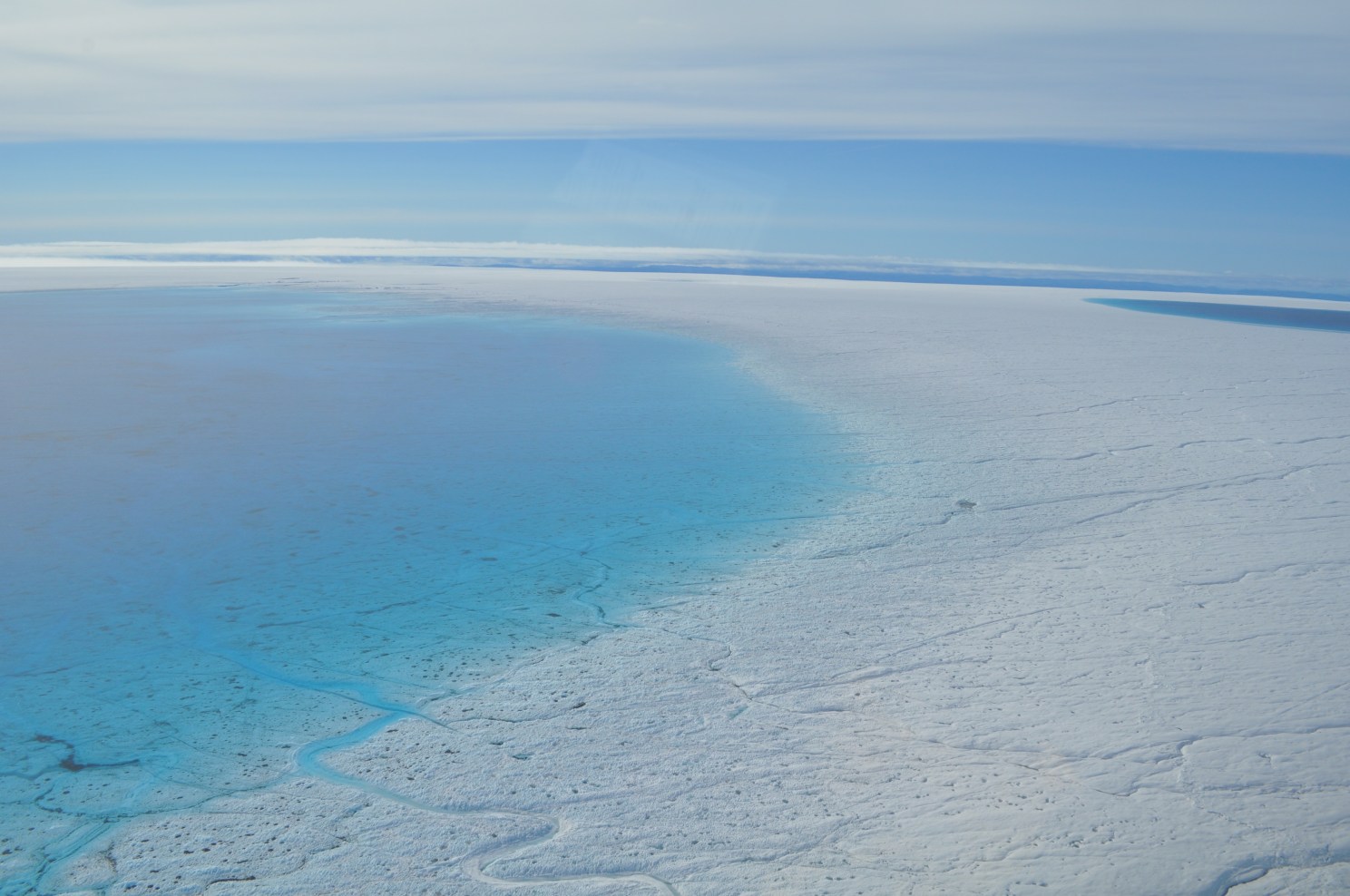 An aerial view of deep blue lakes and streams on the surface of the Greenland Ice Sheet.