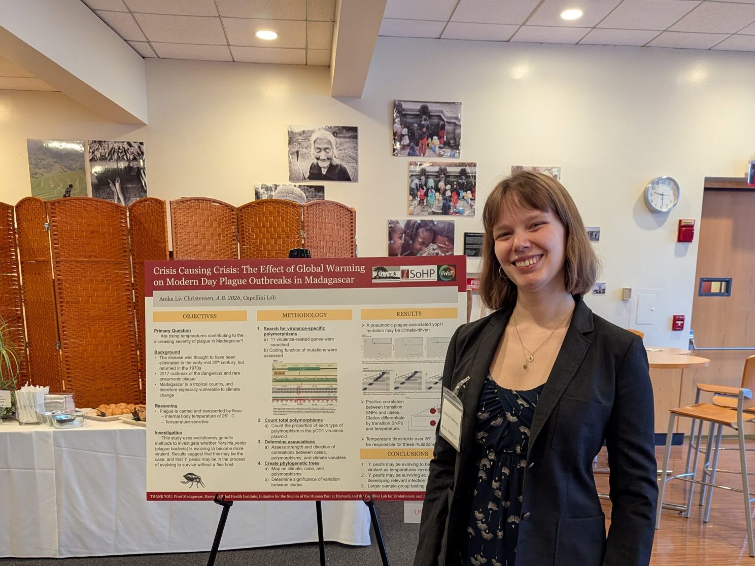 A young woman wearing a dark blazer, standing in front of her research poster.