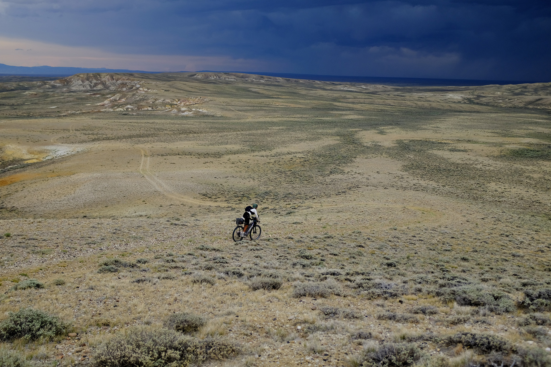 Cyclist George Usmanov riding Wyoming’s Great Divide Basin under dark clouds.
