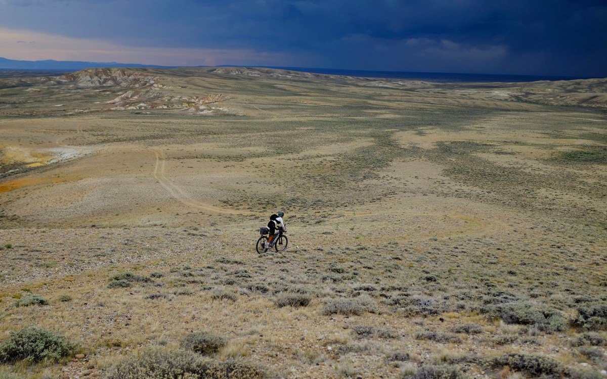 Cyclist George Usmanov riding Wyoming’s Great Divide Basin under dark clouds.