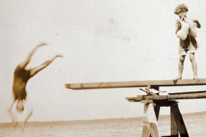 A detail from the family photo archive of Robin Kelsey of a person jumping off a diving board into a lake.