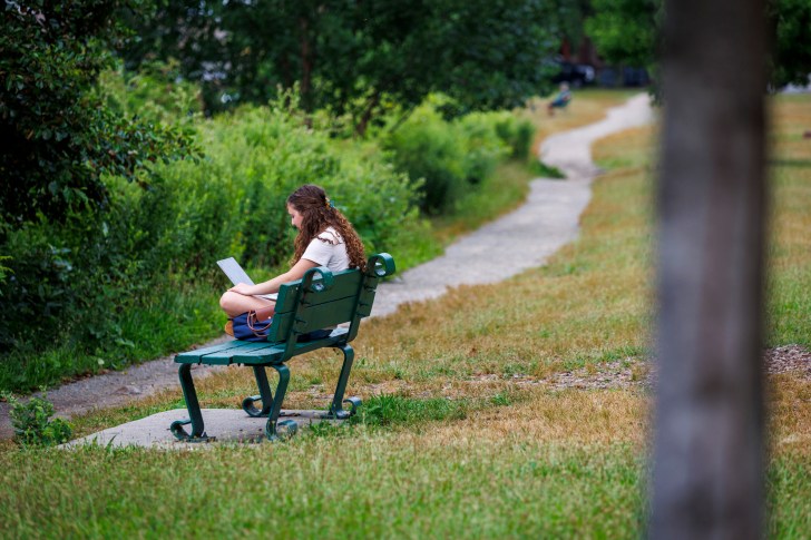 Harvard Summer School student Ellie Stallings sits along the Charles River to do her classwork.