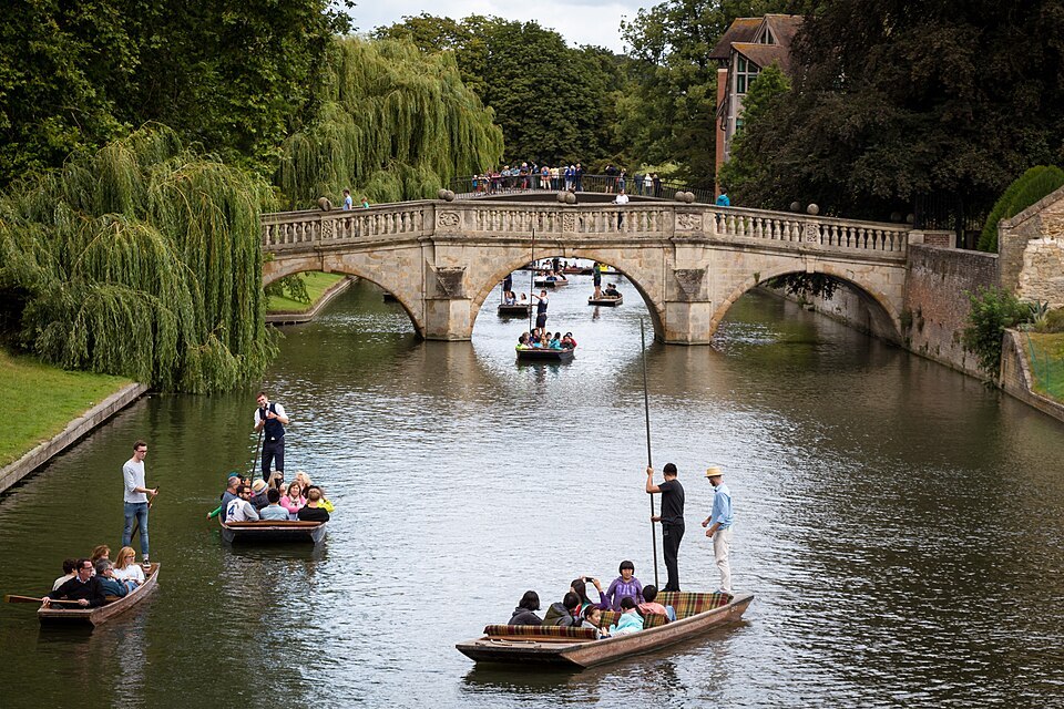 People riding in punts, or flat-bottomed boats, alongside Clare College Bridge in Cambridge, England.