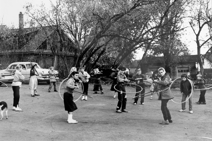 A black and white photograph of a group of children hula-hooping