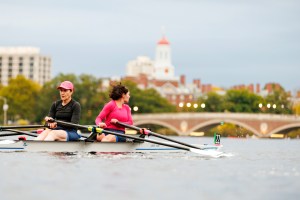 Two rowers head towards the John W. Weeks Footbridge with Dunster House visible in the background.